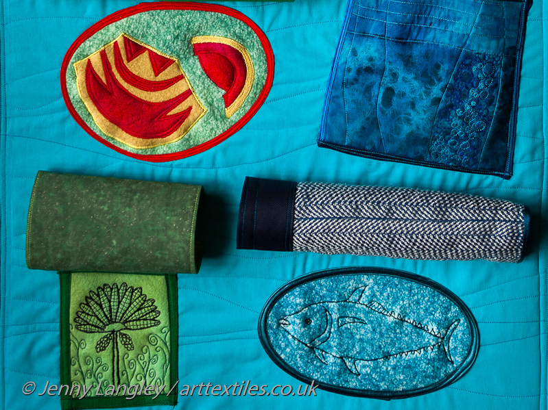 Patch with feather helmet and cape given to Captain Cook.  Centre of the covering flap has a tweeter, which imitates a bird's call when pressed.  Water pocket with crinkly fabric. Flaps rolled up to show a Bonano tree and Albicore fish. 